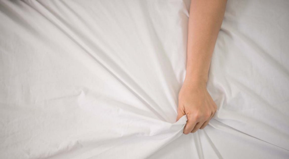 Una mano de mujer sujeta la sábana de la cama